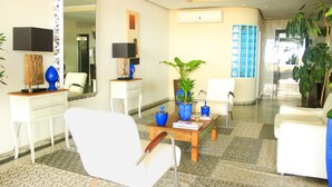 Un moderno vestíbulo de hotel con un sillón blanco, una mesa de centro con libros, un espejo y plantas en macetas.
