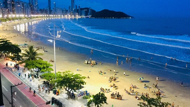 Una playa con gente y vendedores, un horizonte urbano al fondo y una carretera paralela a la playa.