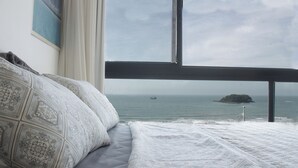 Un dormitorio con un ventanal que da al mar, una cama con ropa de cama estampada y una vista de una isla distante.