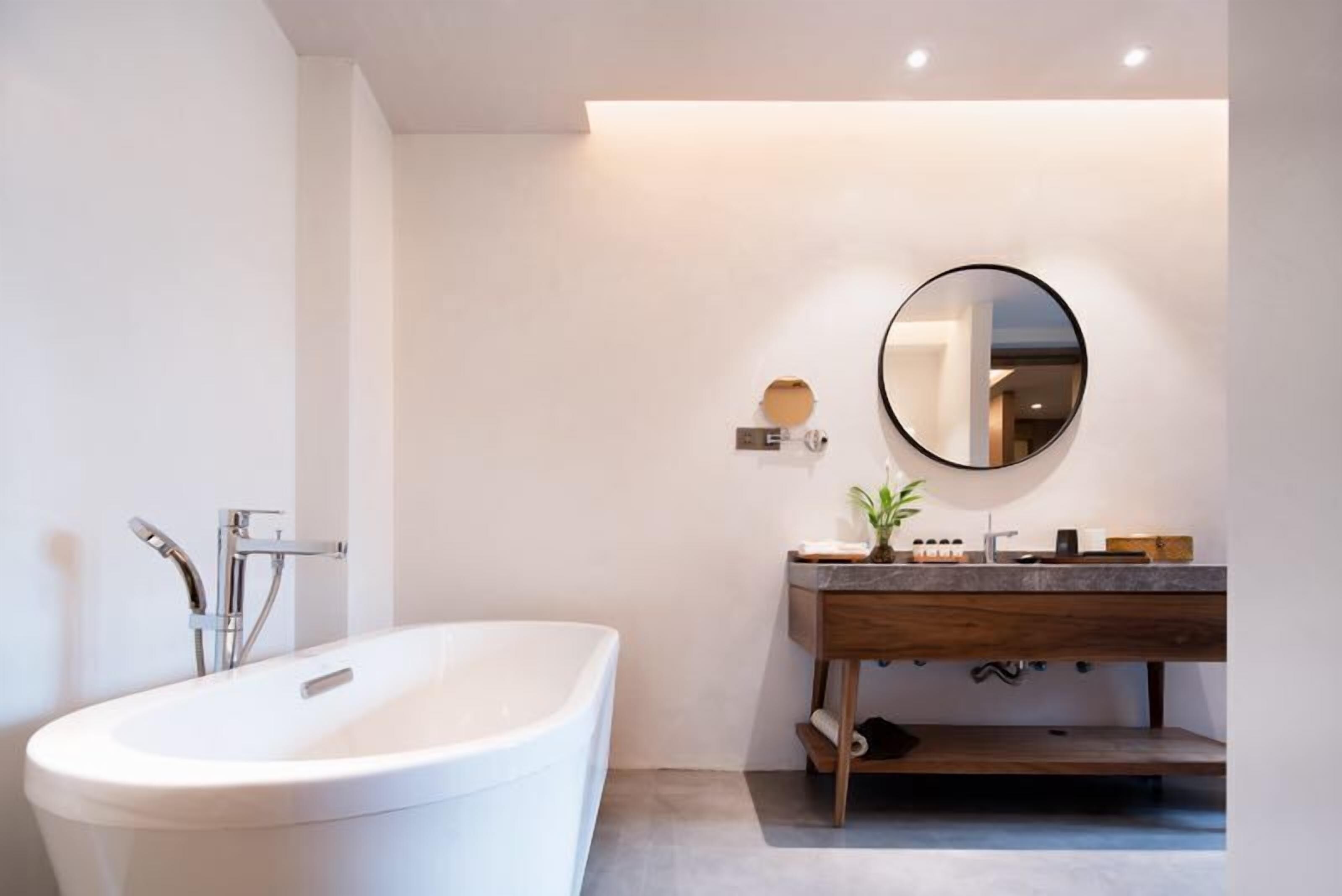 A modern bathroom with a freestanding bathtub, a wooden vanity, and a round mirror.