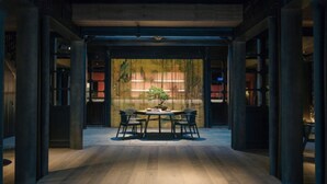 Ein modernes Interieur mit einem zentralen Tisch und Stühlen, umgeben von dunklen Säulen und einem Holzboden.