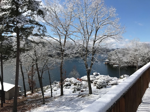 Cubierta nevada con vista a un lago, árboles y un edificio pequeño.