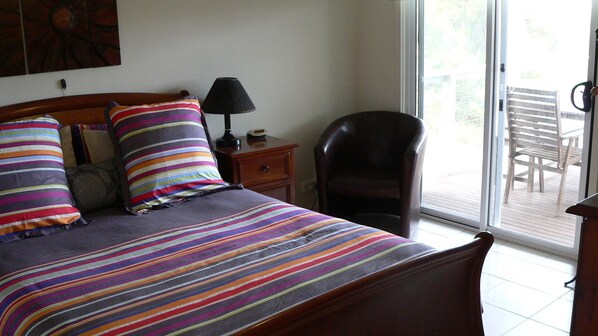 A bedroom with a bed, a nightstand, a lamp, a chair, and a view of the outdoors.