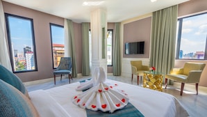 Quarto de hotel com cama, televisão, vista da cidade e janela com cortinas.