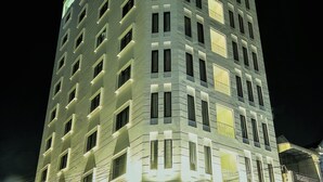 Hotel com vários andares e design moderno, destacando uma entrada imponente com uma placa e fachada bem iluminada.