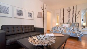 A modern living room with a dark brown sofa, a coffee table with a decorative metal centerpiece, a patterned sofa bed, and framed artwork on the walls. - Quiet Flat. Vibrant Neighborhood! Walk to Pike Place, great restaurants & more. (Seattle)