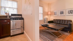 A modern kitchen with a stove, oven, and refrigerator, a living room with a sofa and a coffee table, and artwork on the wall. - Quiet Flat. Vibrant Neighborhood! Walk to Pike Place, great restaurants & more. (Seattle)