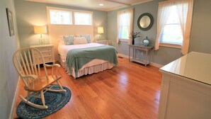 Une chambre à coucher comprenant un lit, un fauteuil à bascule, des tables de chevet et une commode.