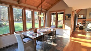 Un espace repas avec une table en bois, des chaises et une vue sur l’extérieur grâce à de grandes fenêtres.