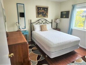 Un dormitorio con cama, cómoda, mesita de noche, lámpara, espejo y ventana con vistas.