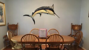 A dining room with a wooden table and chairs, a decorative fish on the wall, and a framed picture.
