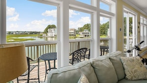A covered outdoor area with a view of a lake and houses, furnished with a sofa, chairs, and a table. - Diving Duck | Waterfront Dock + Hot Tub w/ Captain's Cove Pools & Golf, Pet Friendly 5BR Retreat (Greenbackville)