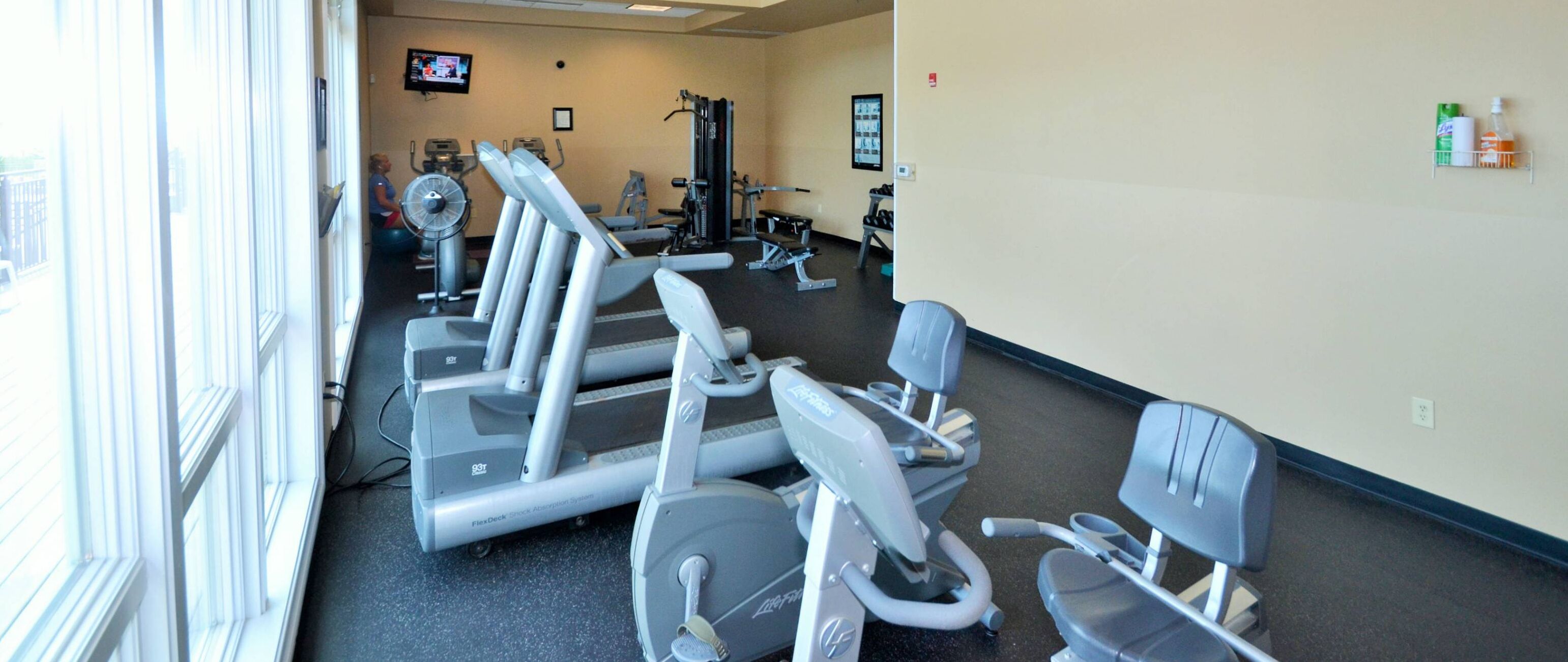 A gym with cardio machines, a TV on the wall, and a shoe rack.