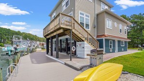 A waterfront property with a wooden deck, a covered outdoor area, and a boat. - Diving Duck | Waterfront Dock + Hot Tub w/ Captain's Cove Pools & Golf, Pet Friendly 5BR Retreat (Greenbackville)