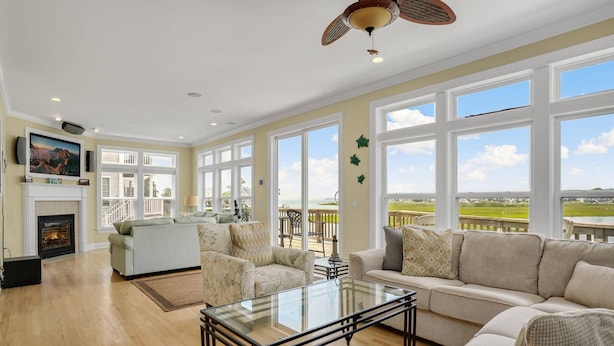A spacious living room with a fireplace, large windows, and a view of the outdoors. - Diving Duck | Waterfront Dock + Hot Tub w/ Captain's Cove Pools & Golf, Pet Friendly 5BR Retreat (Greenbackville)