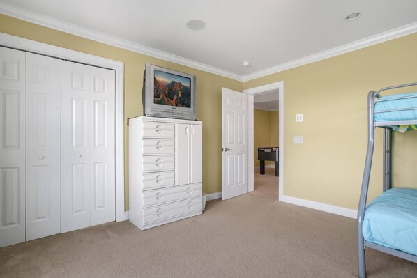 A bedroom with a bunk bed, a white dresser, a television on top, and a door leading to another room.