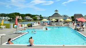 A swimming pool with lounge chairs and umbrellas, surrounded by a dock and houses. - Diving Duck | Waterfront Dock + Hot Tub w/ Captain's Cove Pools & Golf, Pet Friendly 5BR Retreat (Greenbackville)