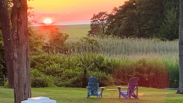 Sonnenuntergangblick von einer Terrasse mit zwei Adirondack-Stühlen, die auf ein Grasfeld und Bäume ausgerichtet sind.