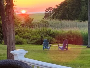 Zonsondergang uitzicht vanaf een terras met twee Adirondack-stoelen, gericht op een grasveld en bomen.
