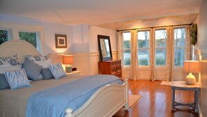 Ein Schlafzimmer mit Bett, Kommode, Nachttischen und einem Fenster mit Vorhängen.