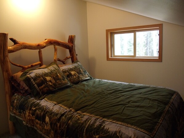 Un dormitorio con una cabecera de madera rústica, un edredón acolchado verde y una ventana con vistas a árboles.