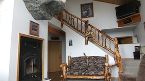 Un salon avec une cheminée, un canapé, une tête d’animal empaillée et un escalier en bois.