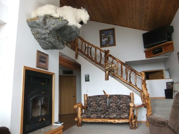 Una sala de estar con chimenea, un sofá, un trofeo de caza y una escalera de madera.
