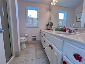 Ein Badezimmer mit Toilette, Dusche, Waschbecken mit Spiegel und einem Fenster mit Jalousien.