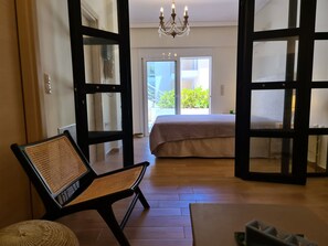 Ein Schlafzimmer mit einem großen Bett, einem Sessel und Blick ins Freie durch eine Glastür.