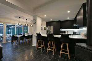 Cozinha moderna com armários pretos, geladeira de aço inoxidável e um balcão com banquetas.