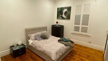 Une chambre à coucher comprenant un lit, une table de chevet, une commode, une fenêtre avec des volets et un tableau accroché au mur.