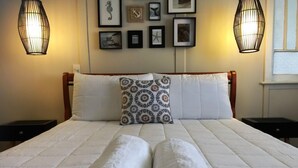 Un lit bien fait, avec du linge de lit blanc et deux serviettes enroulées, un coussin à motifs et un mur décoré de tableaux encadrés.