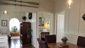 Un coin repas avec une table en bois et des chaises violettes, une plante en pot posée sur la table, et un couloir menant à une chambre.