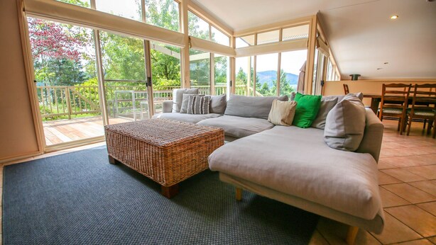 Uma sala de estar espaçosa com um sofá grande, um banquinho de vime e vista para um jardim através de grandes janelas.