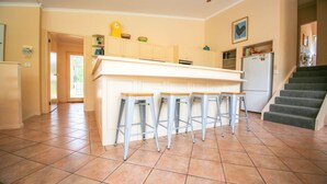 Uma cozinha com ilha central, quatro banquetas, uma geladeira e uma escada.