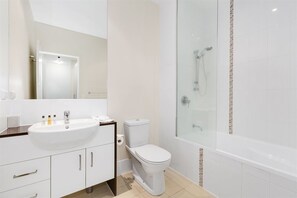 A modern bathroom with a white sink, toilet, and glass-enclosed shower. - 3 Bedroom Executive Rooftop Apartment (Casuarina)