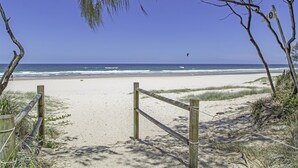 A beach entrance with a wooden gate, sandy path, and beach vegetation.