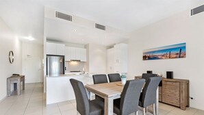 A modern kitchen with white cabinets, a stainless steel refrigerator, and a dining area with a wooden table and four chairs.