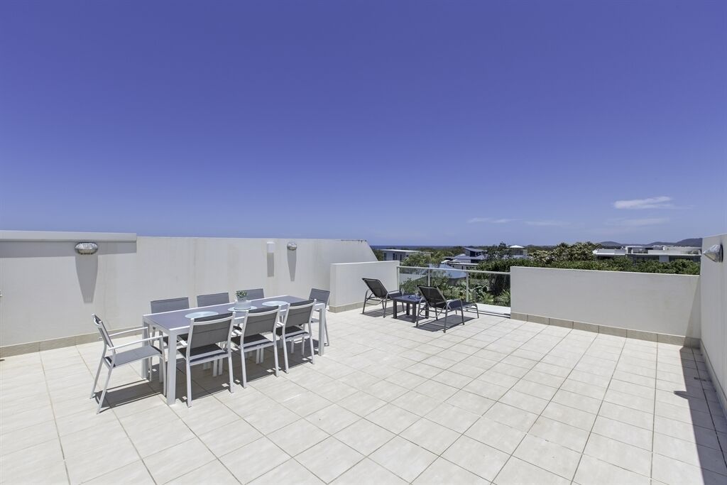 Eine Dachterrasse mit Esstisch und Stühlen, ein kleiner Tisch mit einem Sessel und Blick auf die Umgebung.
