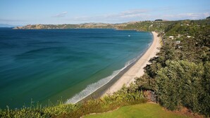 Eine Küstenansicht mit Strand, Grünflächen und Hügeln im Hintergrund.