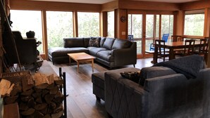 A spacious living area with a sectional sofa, a small coffee table, and a fireplace. There is a dining table with chairs and a large window providing natural light.