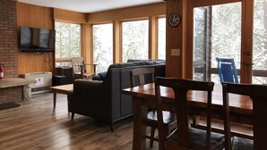 A cozy living area with a fireplace, a television mounted on the wall, and large windows offering a view of the outdoors.