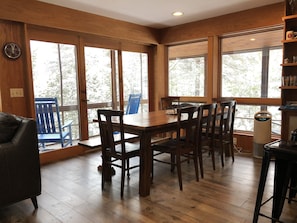 Un coin repas en bois avec une table et des chaises, de grandes fenêtres et une chaise bleue à l’extérieur.