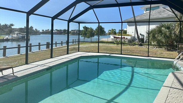 A pool with a clear view of a lake and a boat dock. - Waterfront home with south facing pool & views over the bay (Marco Island)