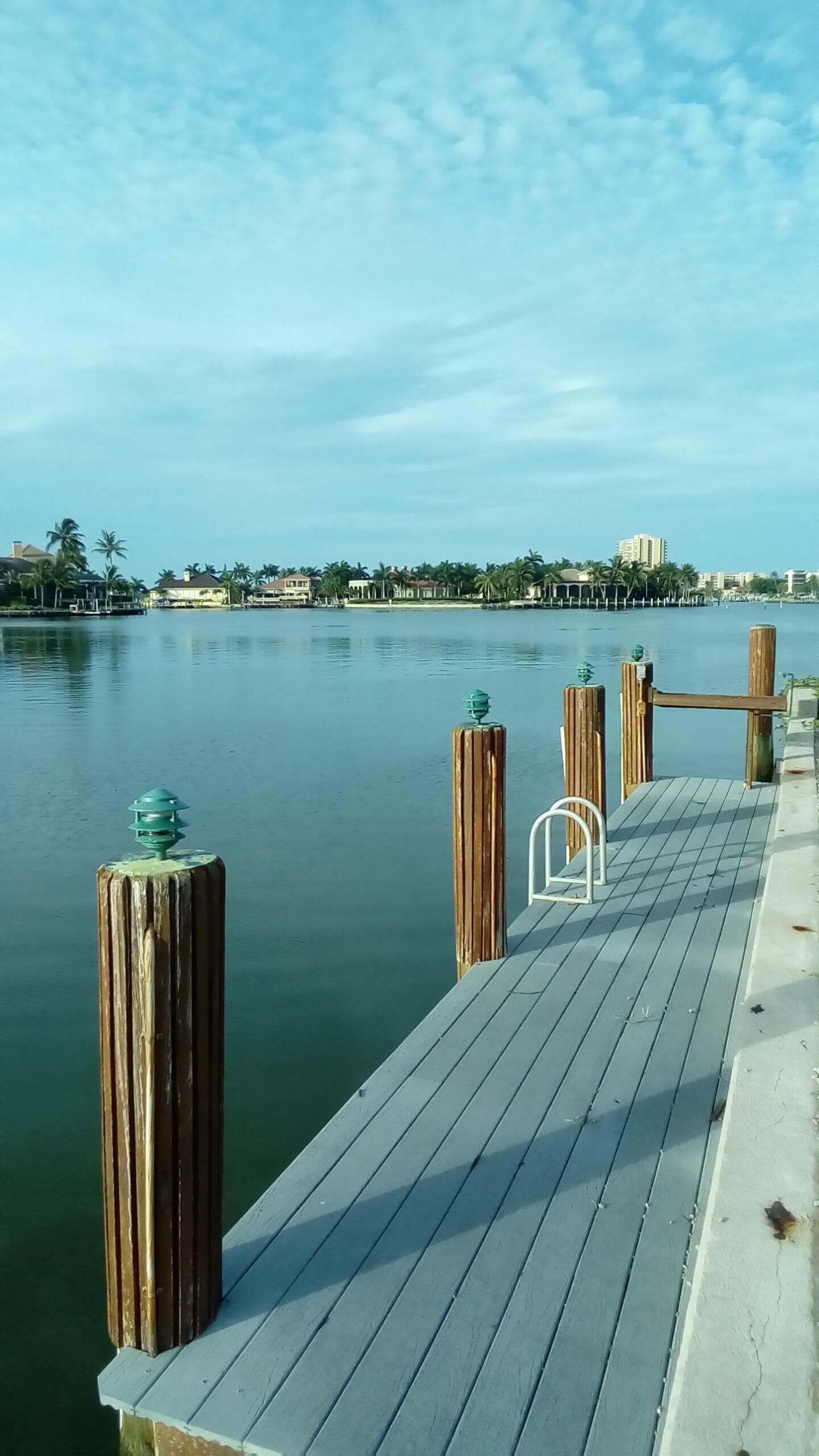 Une jetée en bois s’étendant sur une étendue d’eau calme, sous un ciel dégagé, avec des bâtiments visibles au loin.
