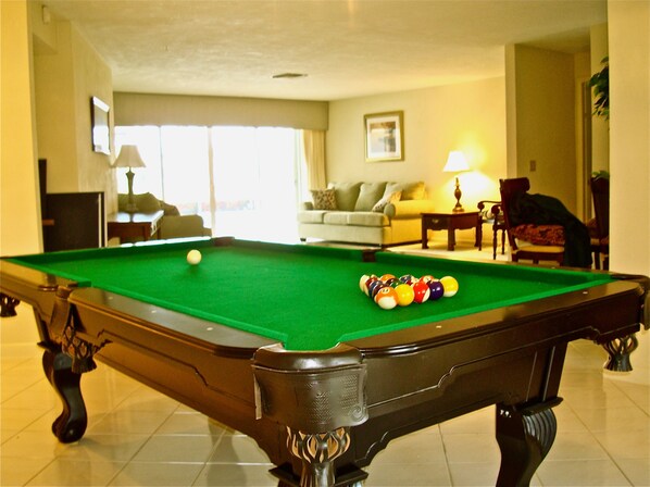 A pool table with balls, a sofa, a lamp, and a chair in a room with a tiled floor.