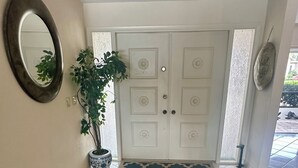 A hallway with a patterned rug, a potted plant, a mirror, and a door with decorative panels. - Waterfront home with south facing pool & views over the bay (Marco Island)