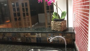 A kitchen with a granite countertop, a stainless steel sink, and a potted plant with pink flowers. - Itaipu Beach House - Ocean View (Itaipu)
