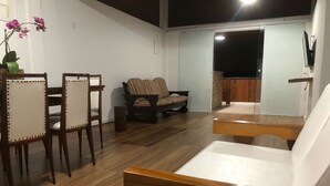 A room with a wooden floor, a dining table with chairs, a sofa, and a TV mounted on the wall. - Itaipu Beach House - Ocean View (Itaipu)