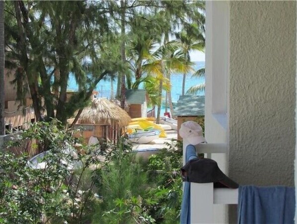 A room with a view of a beach, including palm trees, a thatched-roof hut, and a yellow lounge chair.
